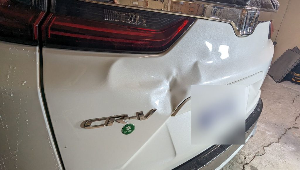 Large dent in the tailgate of a white Honda CR-V before paintless dent repair