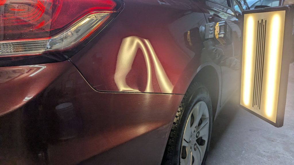 Rear quarter panel dent on a burgundy hatchback under the PDR light