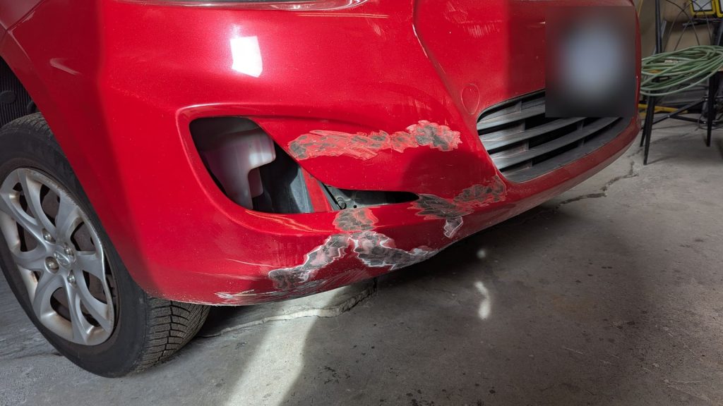 Scraped and cracked front bumper on a red Hyundai Accent before body repair