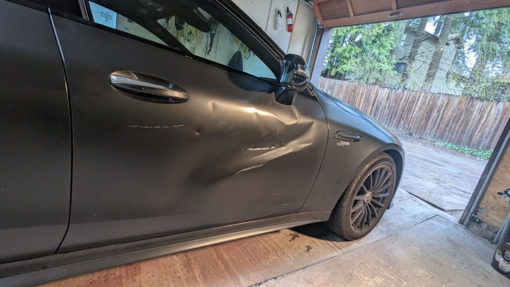 Large dent along the driver door of a grey Mercedes-AMG GT before paintless dent repair
