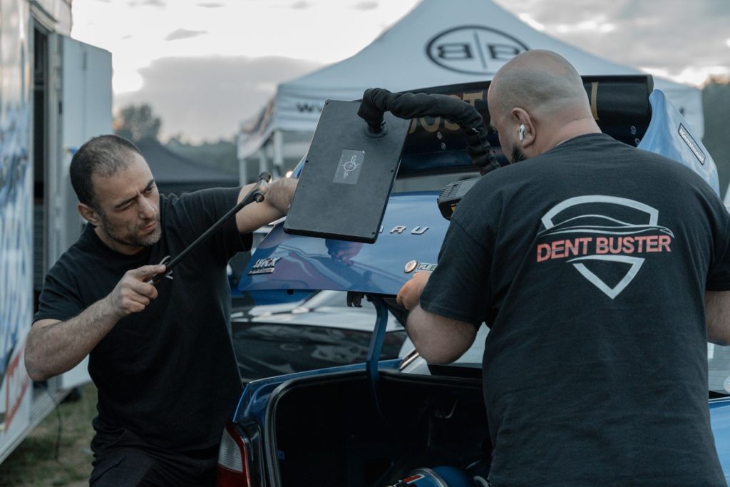 Mobile repair on a blue Subaru at a car show