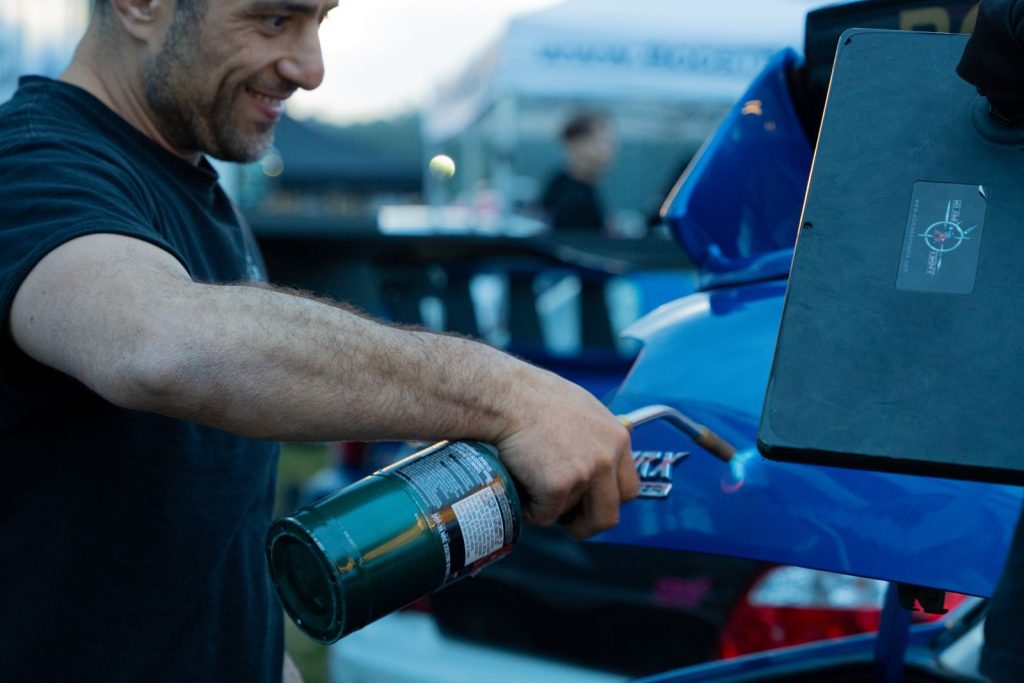 Technician warming a Subaru trunk lid with a torch during paintless dent repair