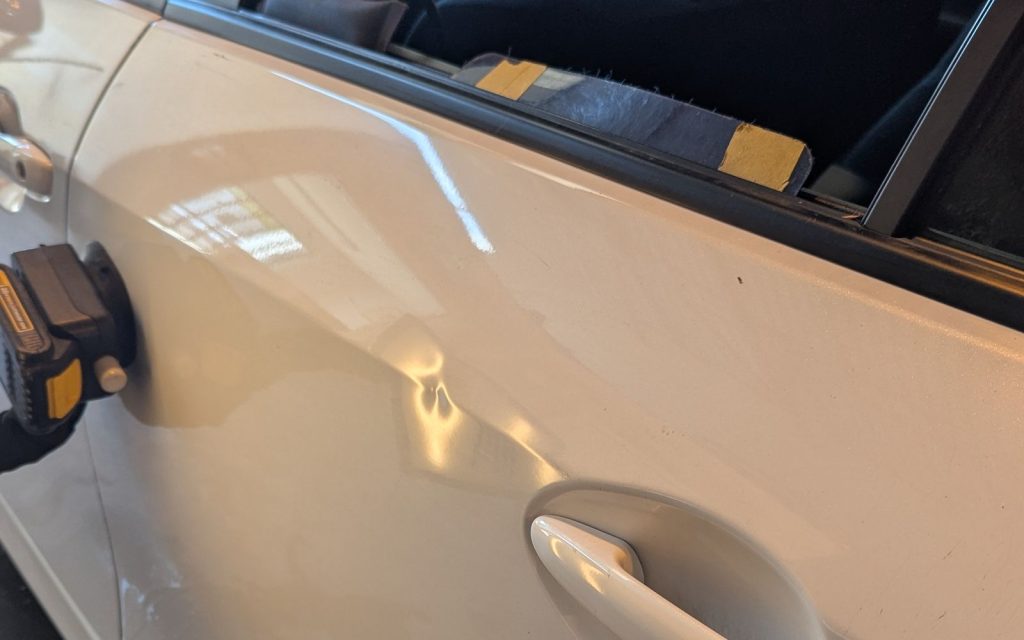 Door ding near the handle of a white car before paintless dent repair