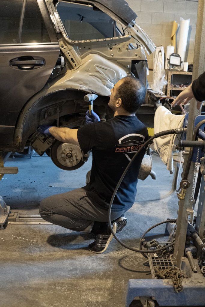 Technician in a Dent Buster shirt reshaping a quarter panel on the frame machine