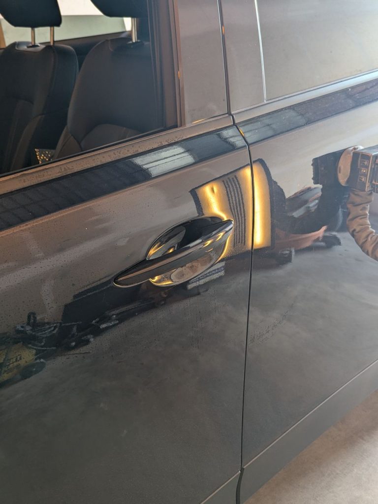 Dent beside the door handle of a dark SUV, reflection lines bent