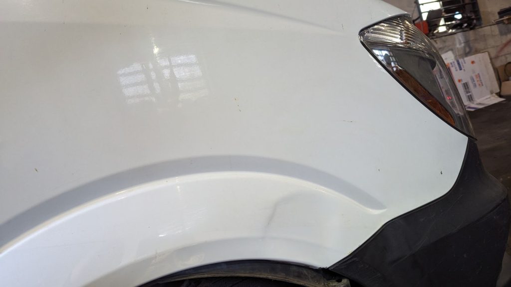 Dent above the front wheel arch of a white SUV before paintless dent repair