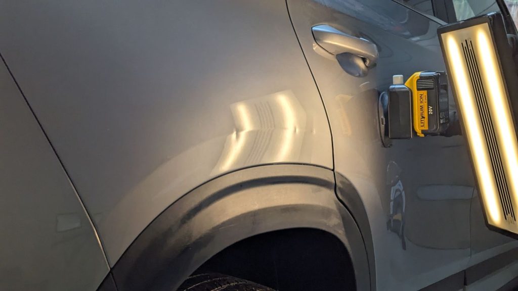Rear quarter panel dent on a grey SUV with reflection lines bent under the PDR light
