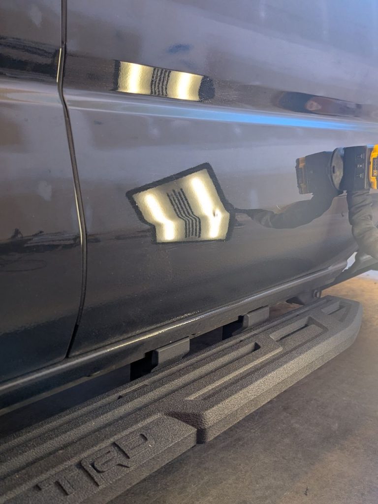Door dent on a grey Toyota Tacoma with reflection lines bent