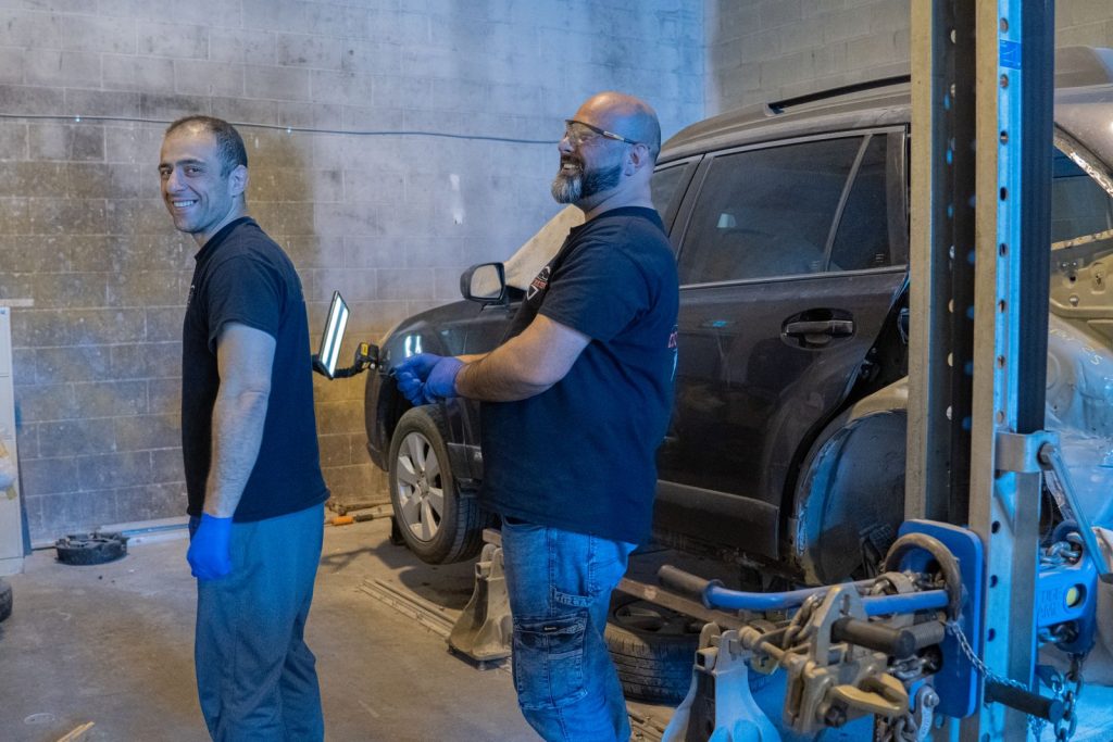 The Dent Buster Autocare team smiling in the Maple Ridge shop beside a Subaru Outback on the frame machine