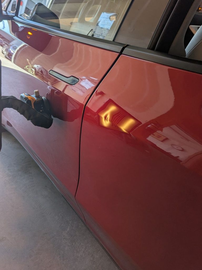 Dent on the rear door of a red Tesla Model Y before paintless dent repair