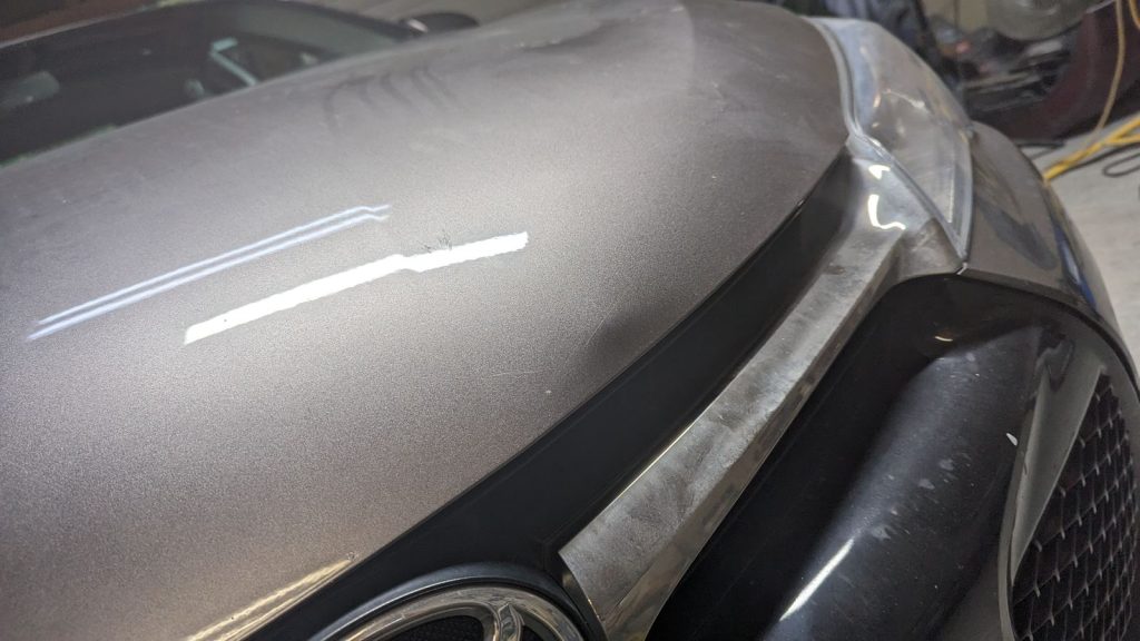 Dent on the front edge of a grey Toyota hood before repair