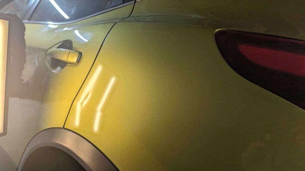 Rear quarter panel dent on a yellow crossover with reflection lines bent
